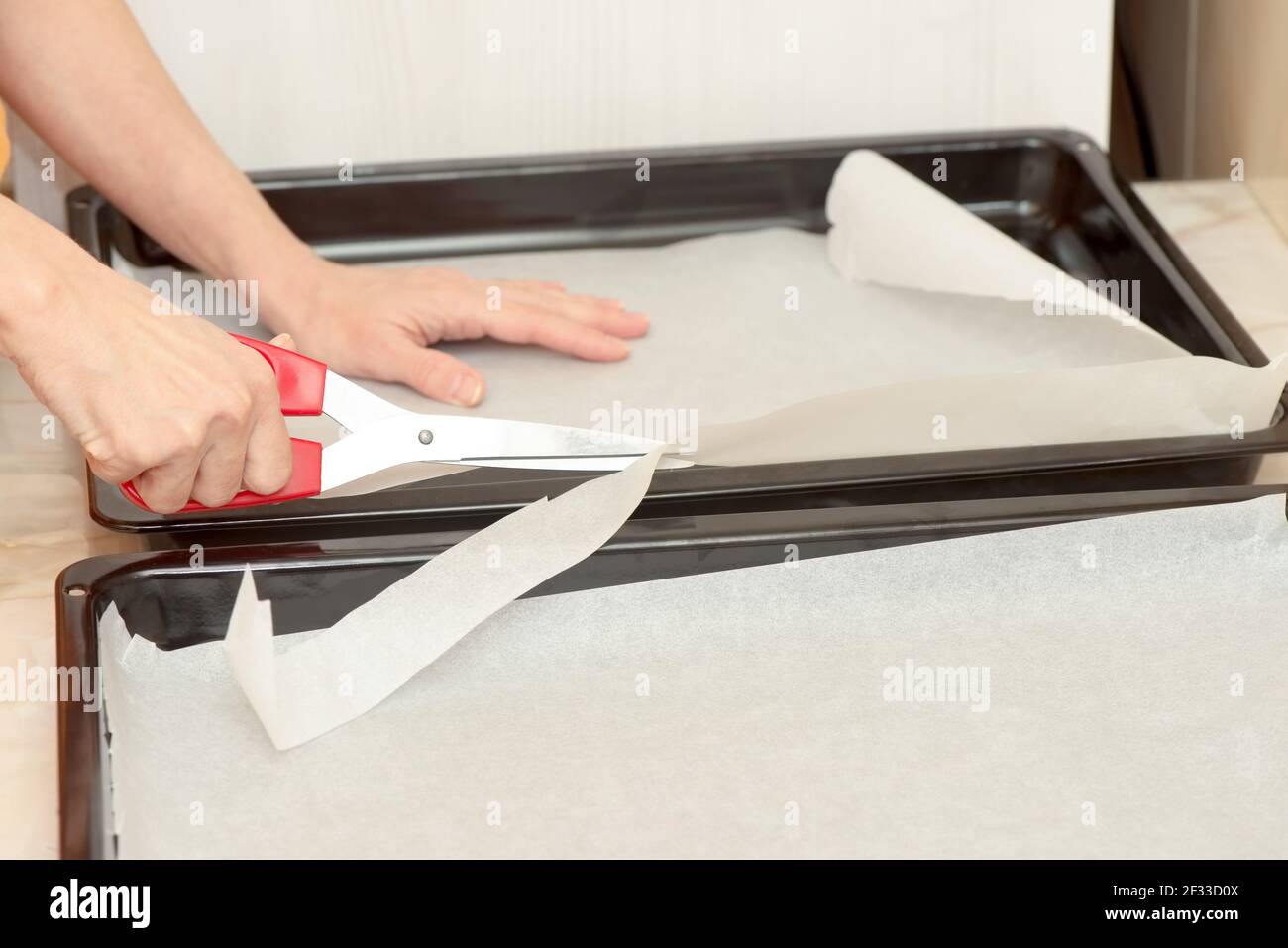 Le mani della donna tagliano la carta da forno con le forbici Foto Stock