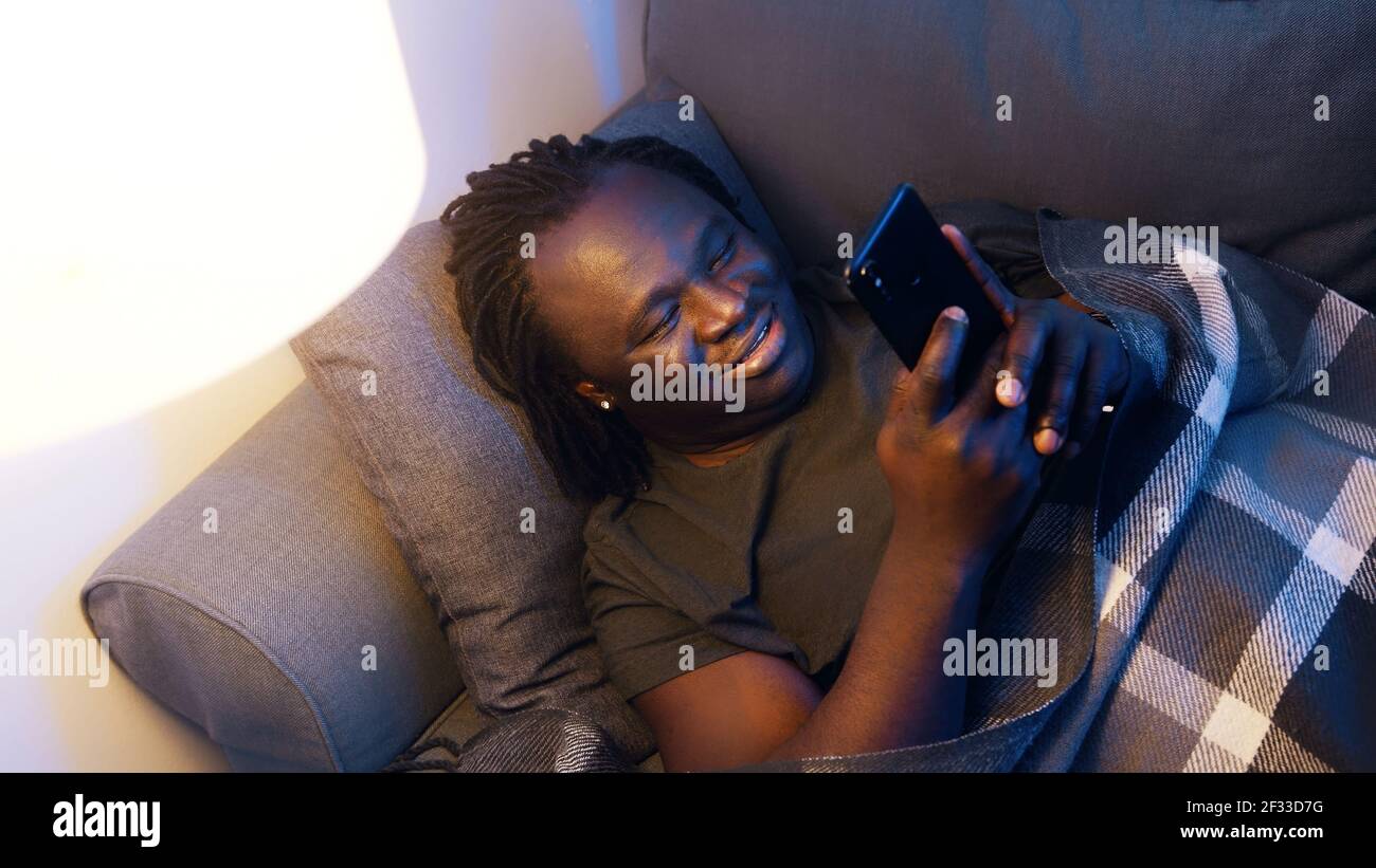 Felice giovane uomo nero sorridente mentre si usa lo smartphone. Connessione durante la quarantena. Foto di alta qualità Foto Stock