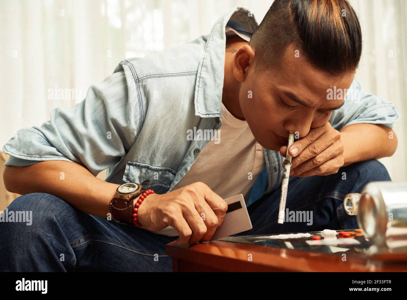 Bell'uomo vietnamita che sniffing la cocaina attraverso la banconota arrotolata a. casa Foto Stock