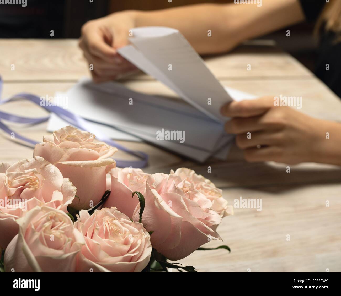 Giovane donna che apre lettere dai suoi cari parenti o amici. Ottenga il regalo per compleanno. Belle rose rosa in primo piano. Foto Stock