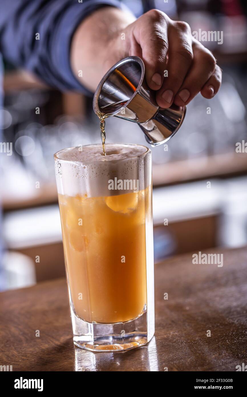 Mano di un barman che versa un liquido nel cocktail con la schiuma sulla parte superiore. Foto Stock