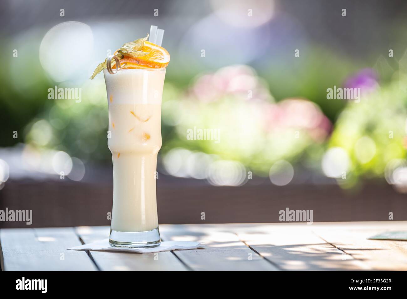 Cocktail PinaColada o Milkshake con padelle e arancio sulla parte superiore servito in un bicchiere alto su una terrazza estiva. Foto Stock
