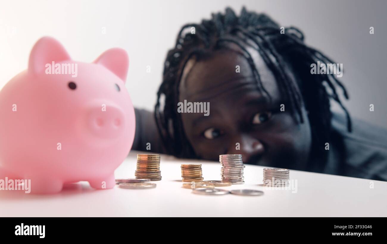 Decisioni finanziarie, investimenti e risparmi. Uomo divertente guardando nelle monete di fronte alla banca piggy. Messa a fuoco della scaffalatura. Foto di alta qualità Foto Stock