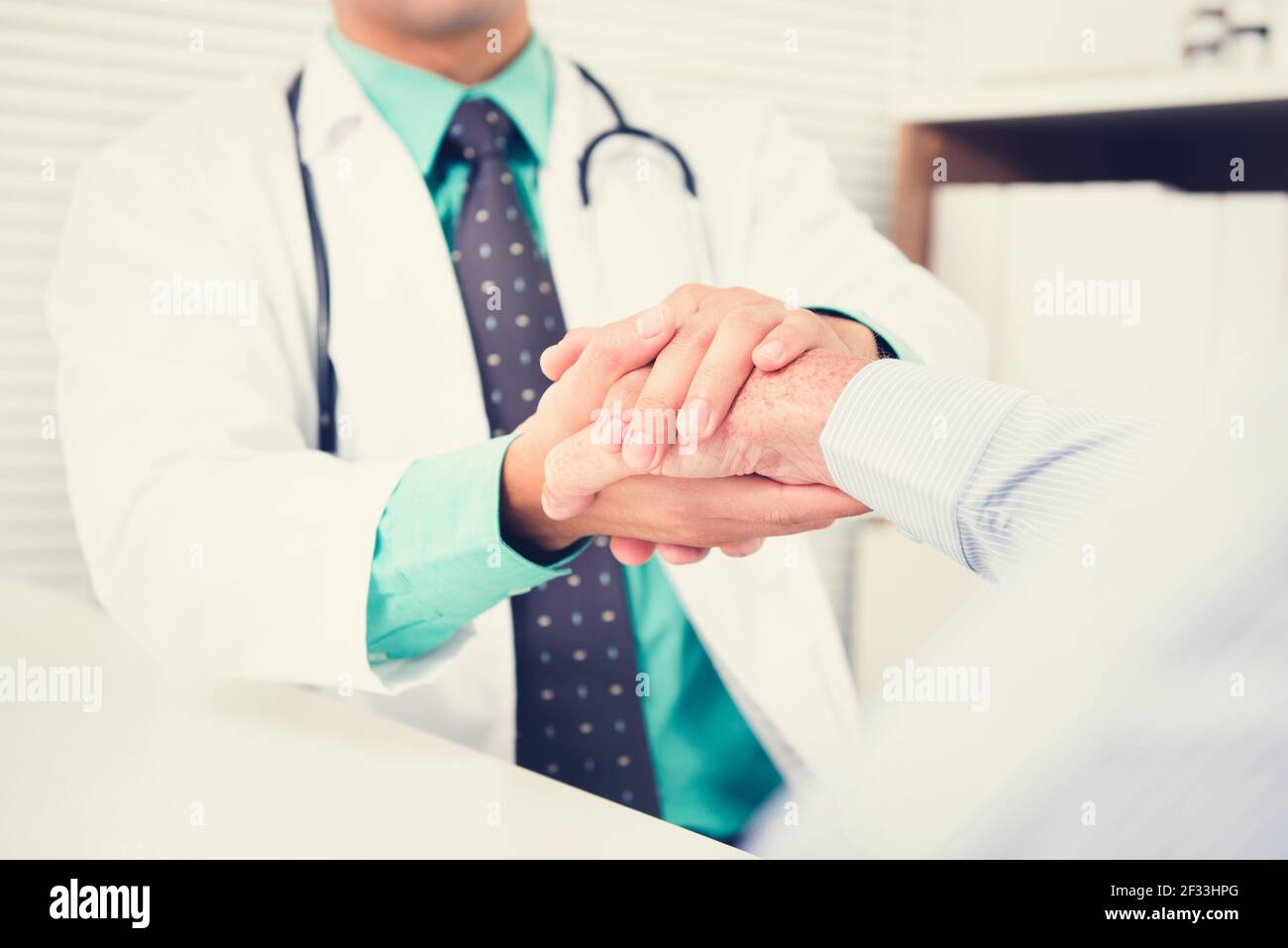 Medico che tiene la mano del paziente maschile senior con cura, effetto tono vintage Foto Stock