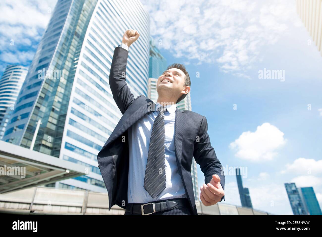 Imprenditore sorridente e sollevando il pugno in aria, con edificio per uffici di sfondo - Il successo aziendale, conseguimento e vincere dei concetti Foto Stock