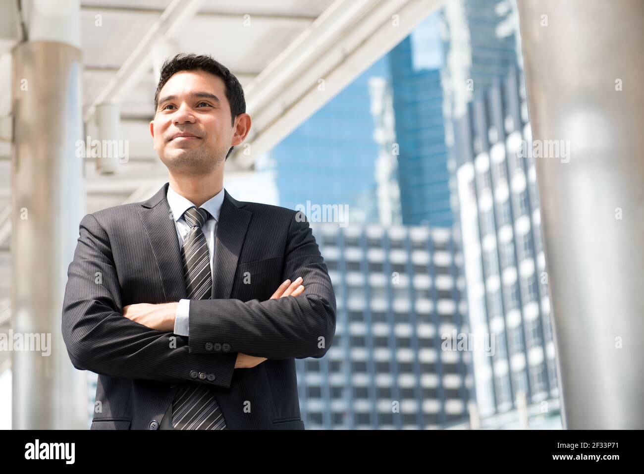 Uomo d'affari asiatico in piedi e incrociando le braccia in blur building sfondo Foto Stock