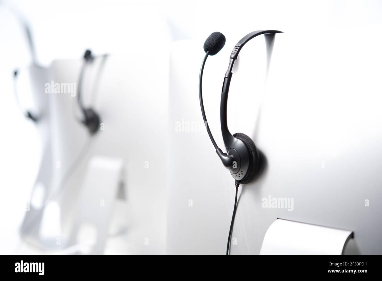 Cuffie con microfono appese sui monitor del computer nel call center Foto Stock