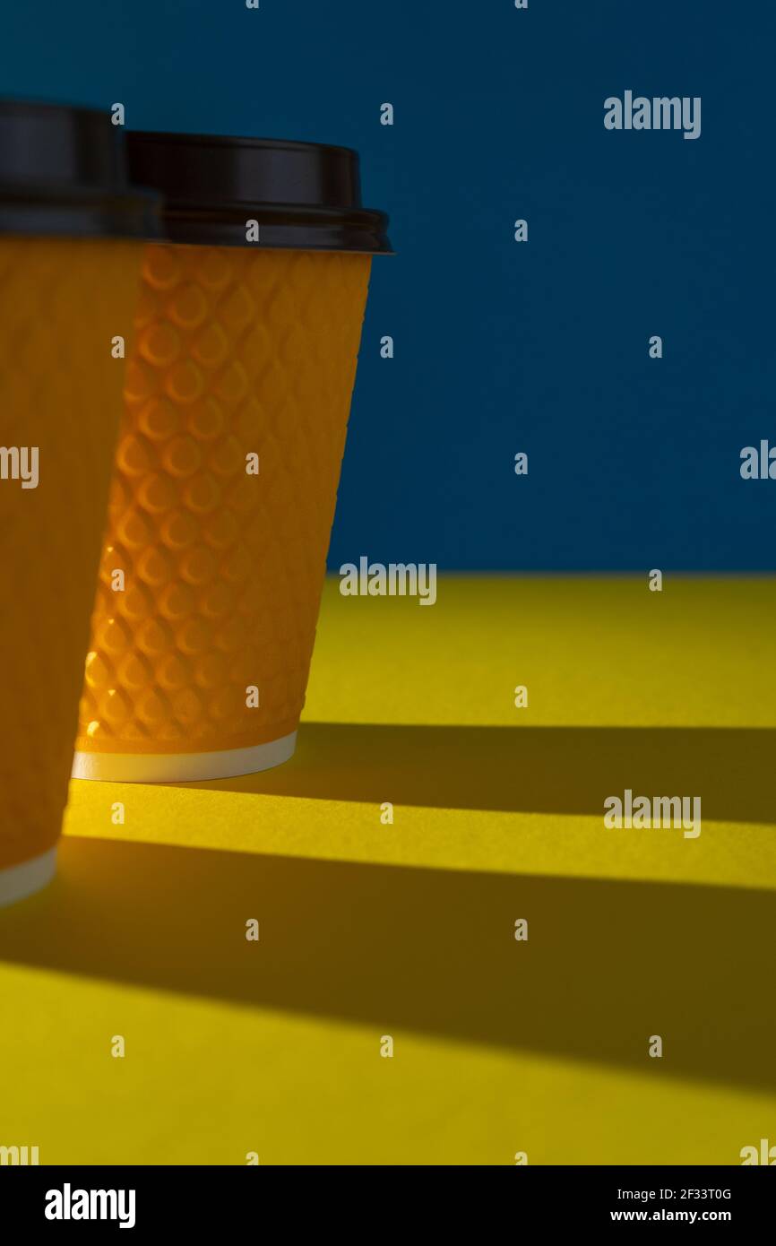 Tazza di carta gialla a coste con coperchio in plastica per bevande da asporto nei fast food. Una tazza di caffè, cioccolata, tè da un caffè in strada. Inserire il testo. Sfondo blu. Foto Stock