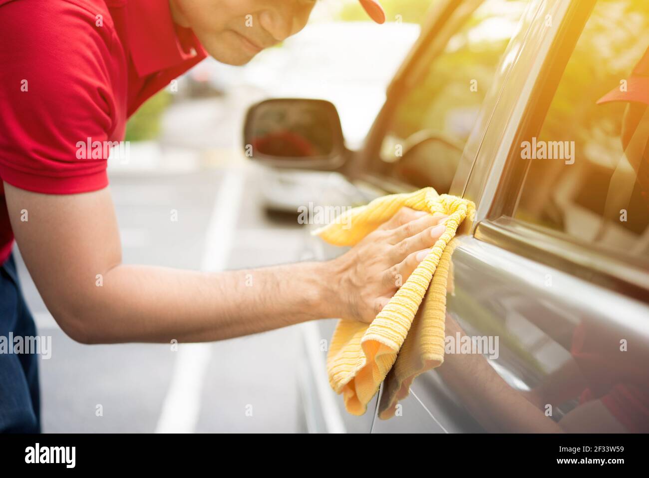 Lavaggio e pulizia auto presso la stazione di servizio auto professionale.  Vista ravvicinata del giovane lavoratore caucasico maschio che pulisce i  fari dell'auto con un panno in microfibra blu utilizzando acqua ad