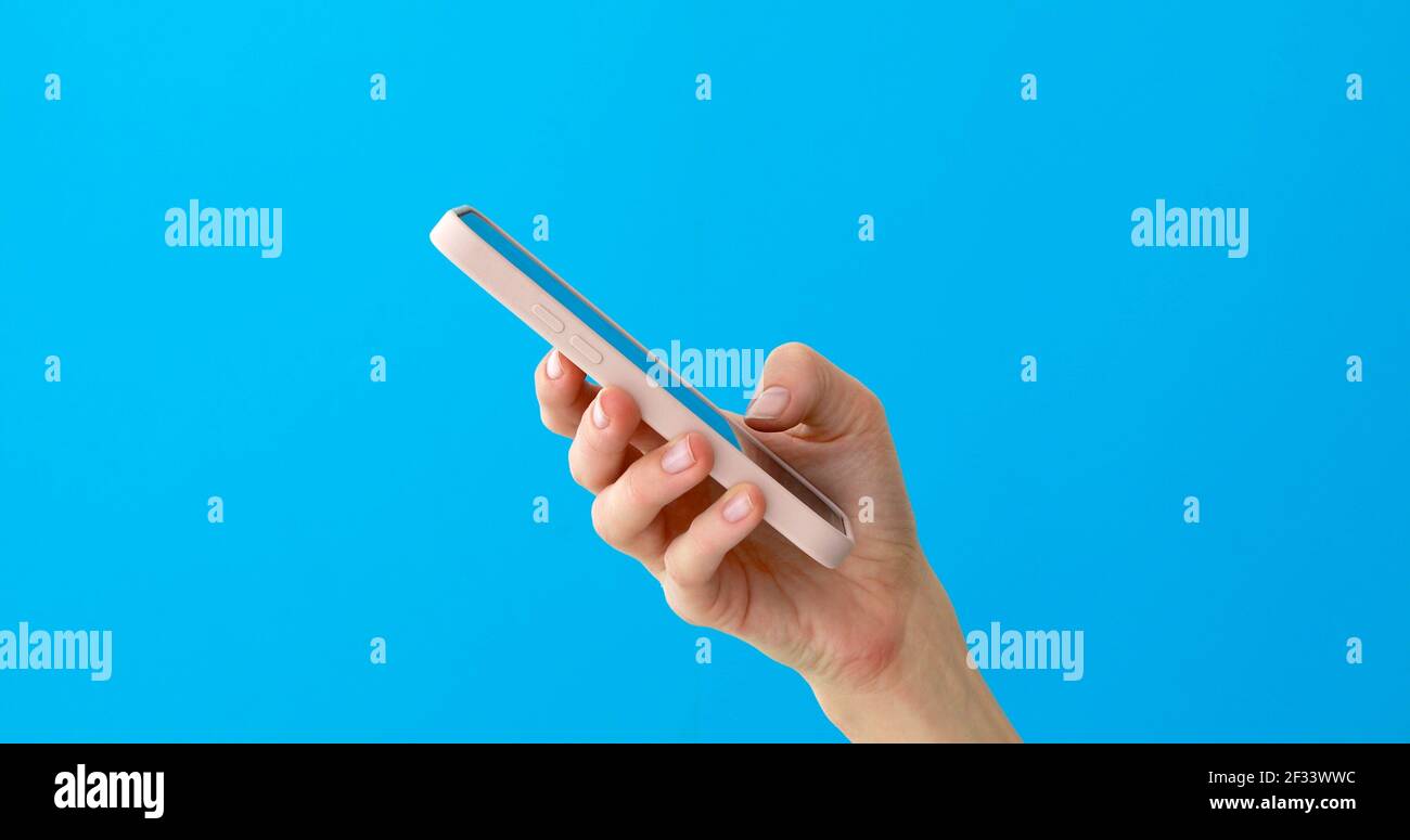 Primo piano della silhouette delle mani della donna utilizzando il touchscreen dello smartphone su sfondo blu. Vista laterale palmo ombra messaggio di digitazione sul telefono cellulare blu retro Foto Stock