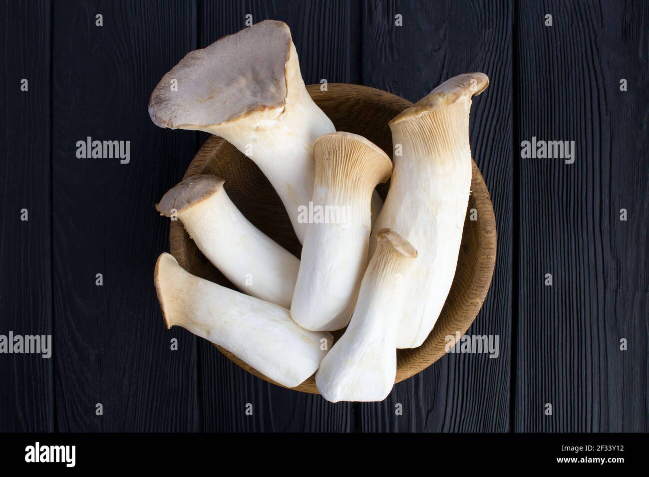 Funghi eringi nella ciotola marrone sullo sfondo di legno nero.Top view.Closeup. Foto Stock