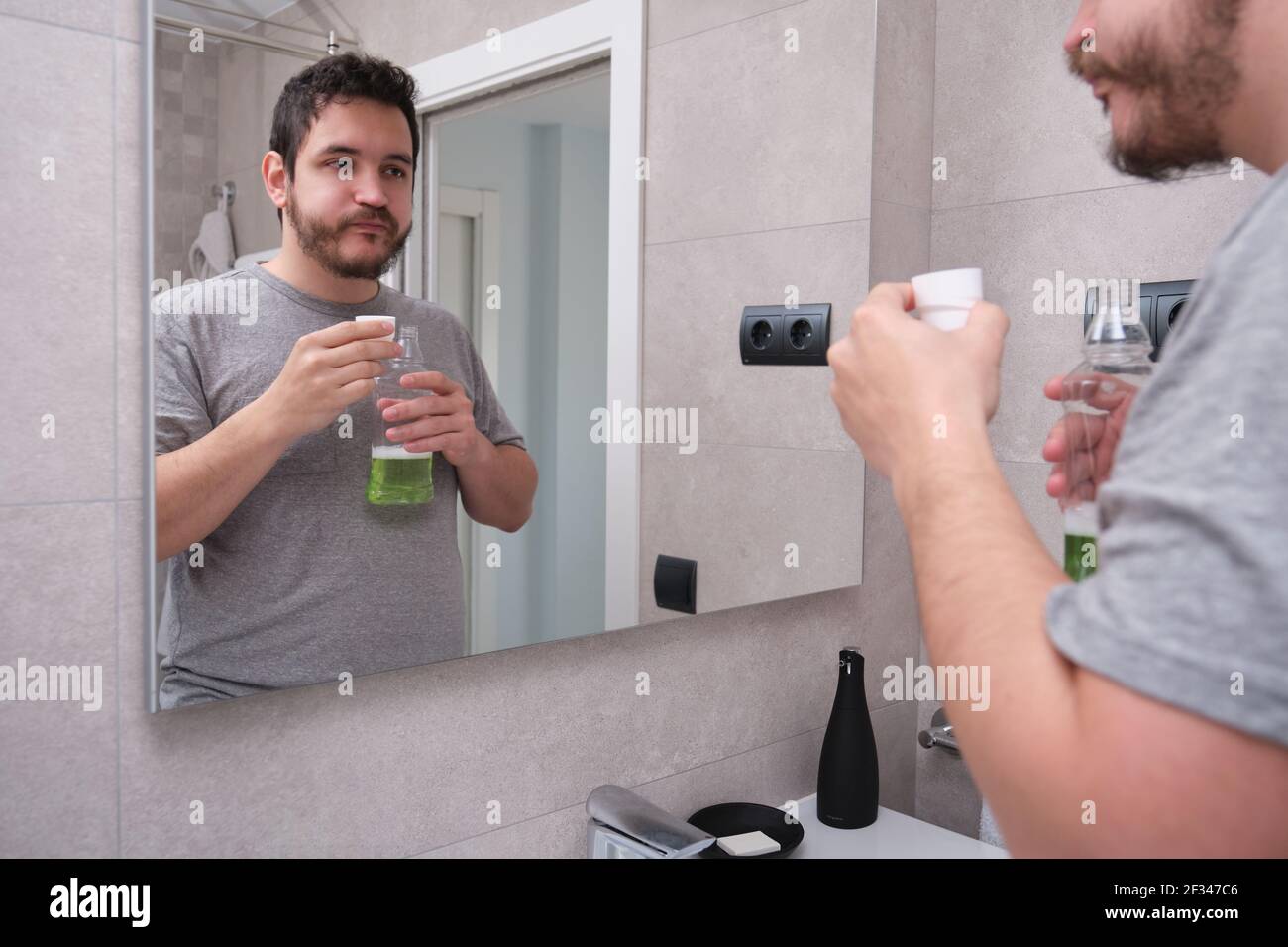 Bocca di risciacquo uomo con collutorio verde in bagno. Concetto di cura dei denti. Foto Stock