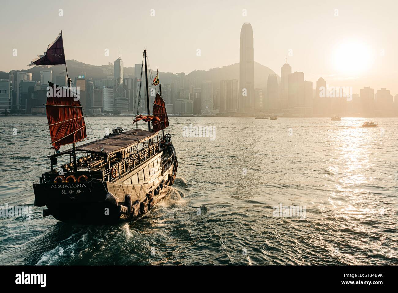 La vista dal molo Tsimshatsui di Kowloon attraverso Victoria Harbour all'Isola di Hong Kong mentre l'Aqua Luna, una giunca tradizionale, salpa Foto Stock