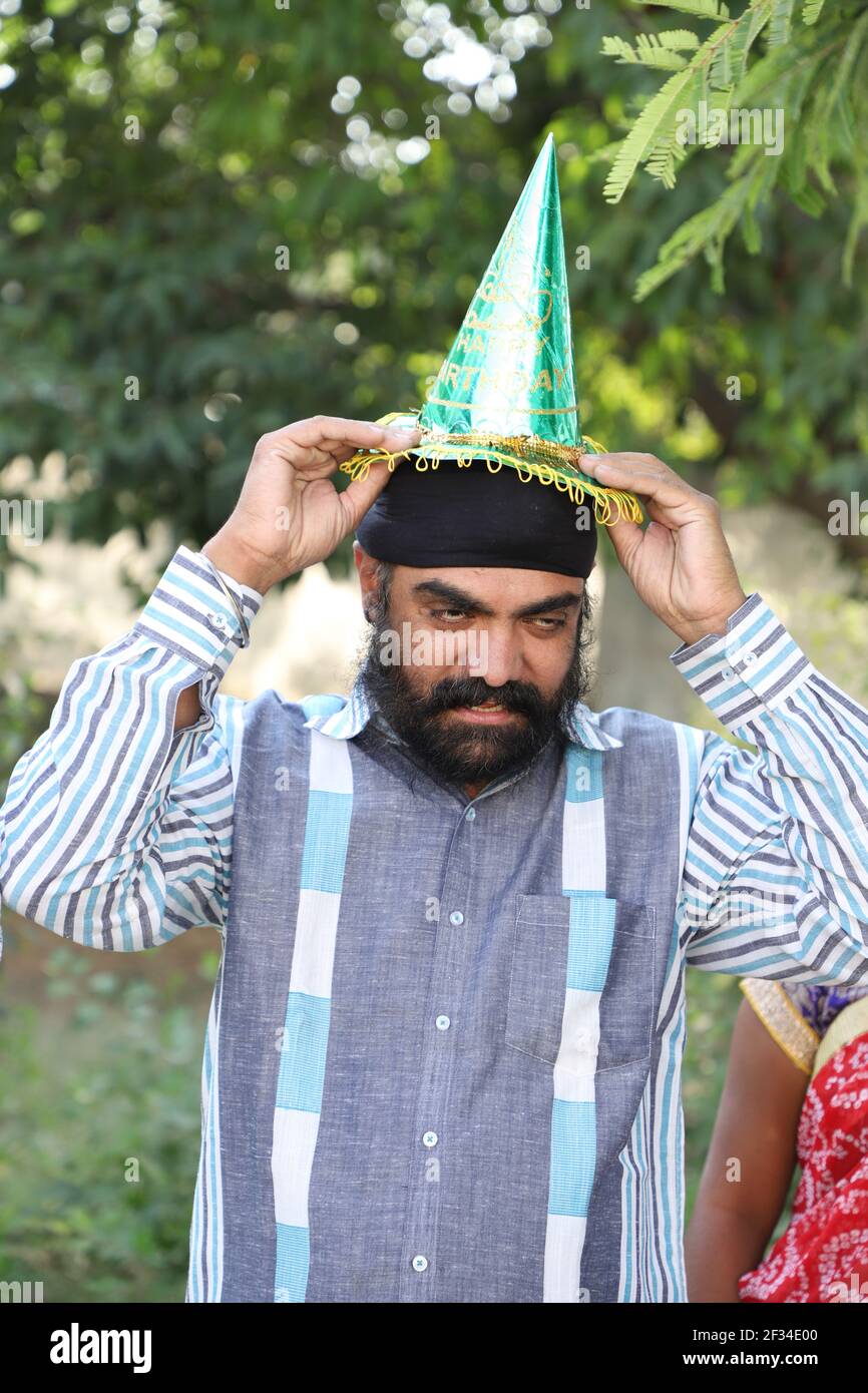 Un indiano di mezza età con un turbante sulla testa cercando di indossare  un cappello di carta per un compleanno Foto stock - Alamy