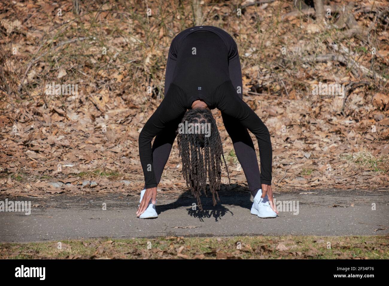 Una donna agile e flessibile negli anni cinquanta conduce una lezione di yoga meditativa quotidiana in un parco a Queens, New York City. Foto Stock