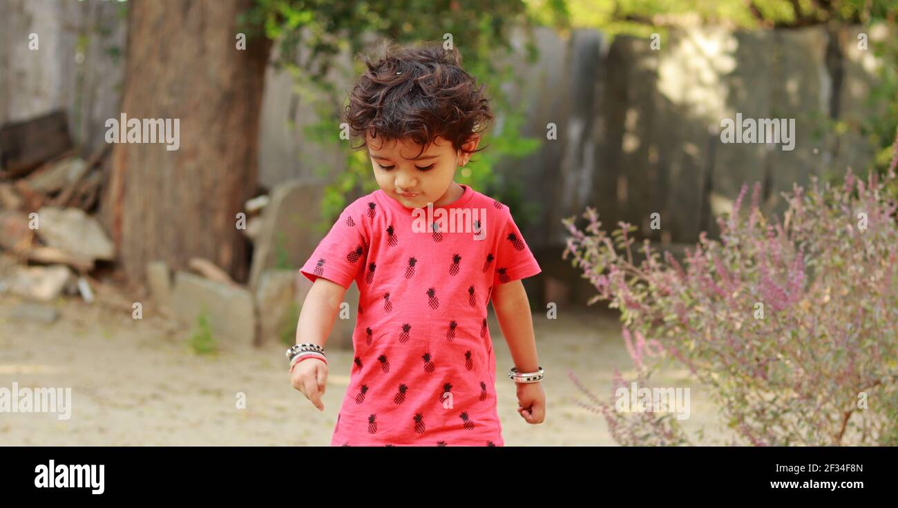 Un bambino di origine indiana che indossa una camicia rossa guardando verso il basso a terra, india.Concept per le gioie dell'infanzia, i ricordi dell'infanzia, il viso del bambino espelle Foto Stock