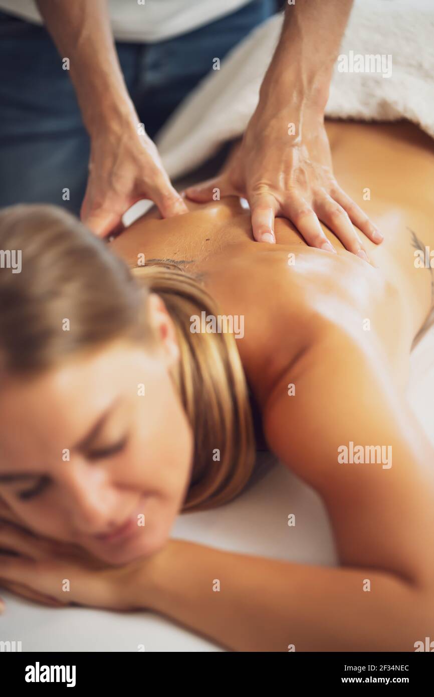 Massaggiatore professionista che fa massaggio terapeutico. Donna che ama il massaggio a casa sua. Giovane donna che ottiene massaggio rilassante del corpo. Foto Stock