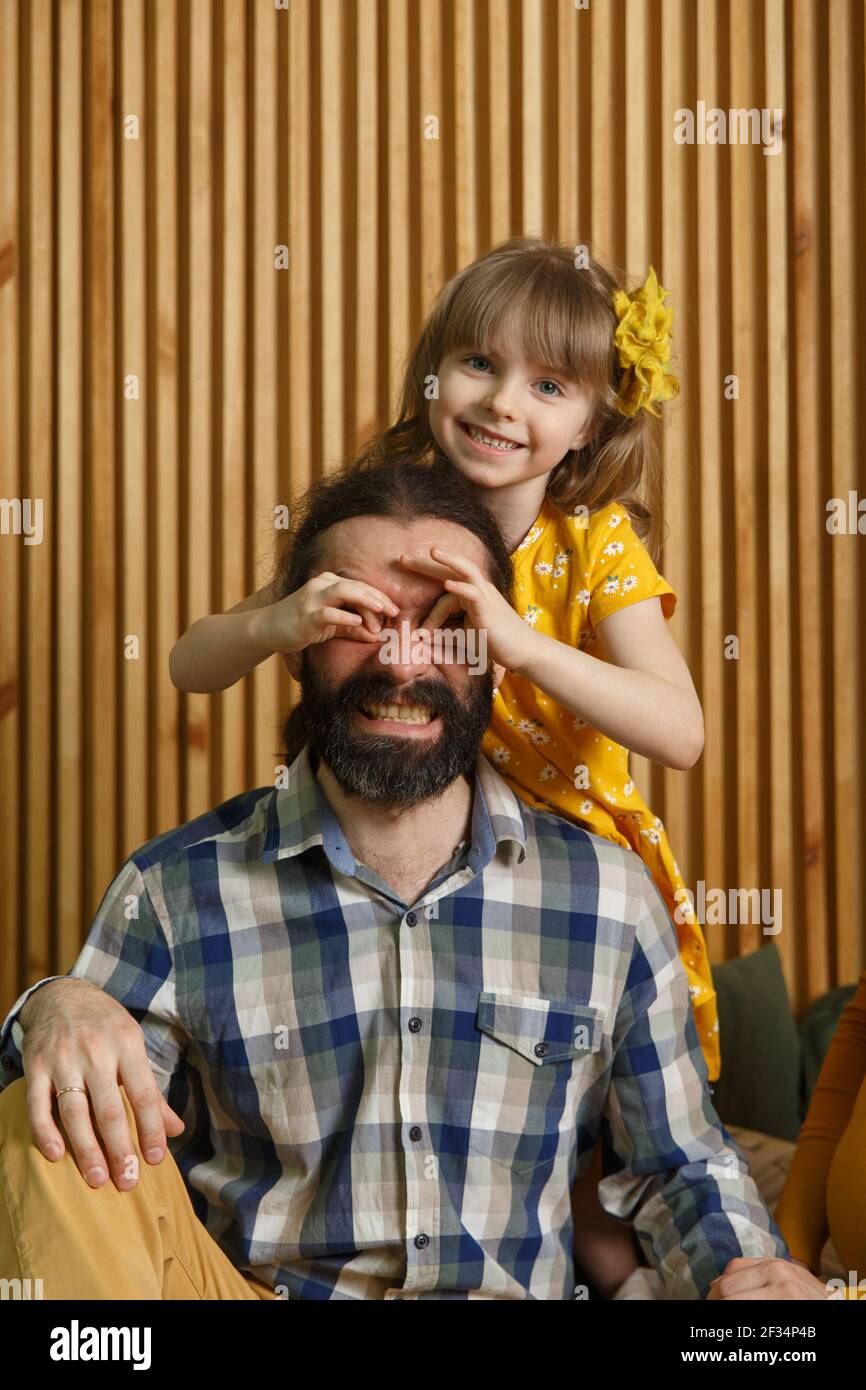 Piccola figlia e padre hanno divertimento a casa, faccia i volti divertenti facendo con le dita eyewear forma come occhiali guardando la macchina fotografica attraverso binocoli, eyegla Foto Stock