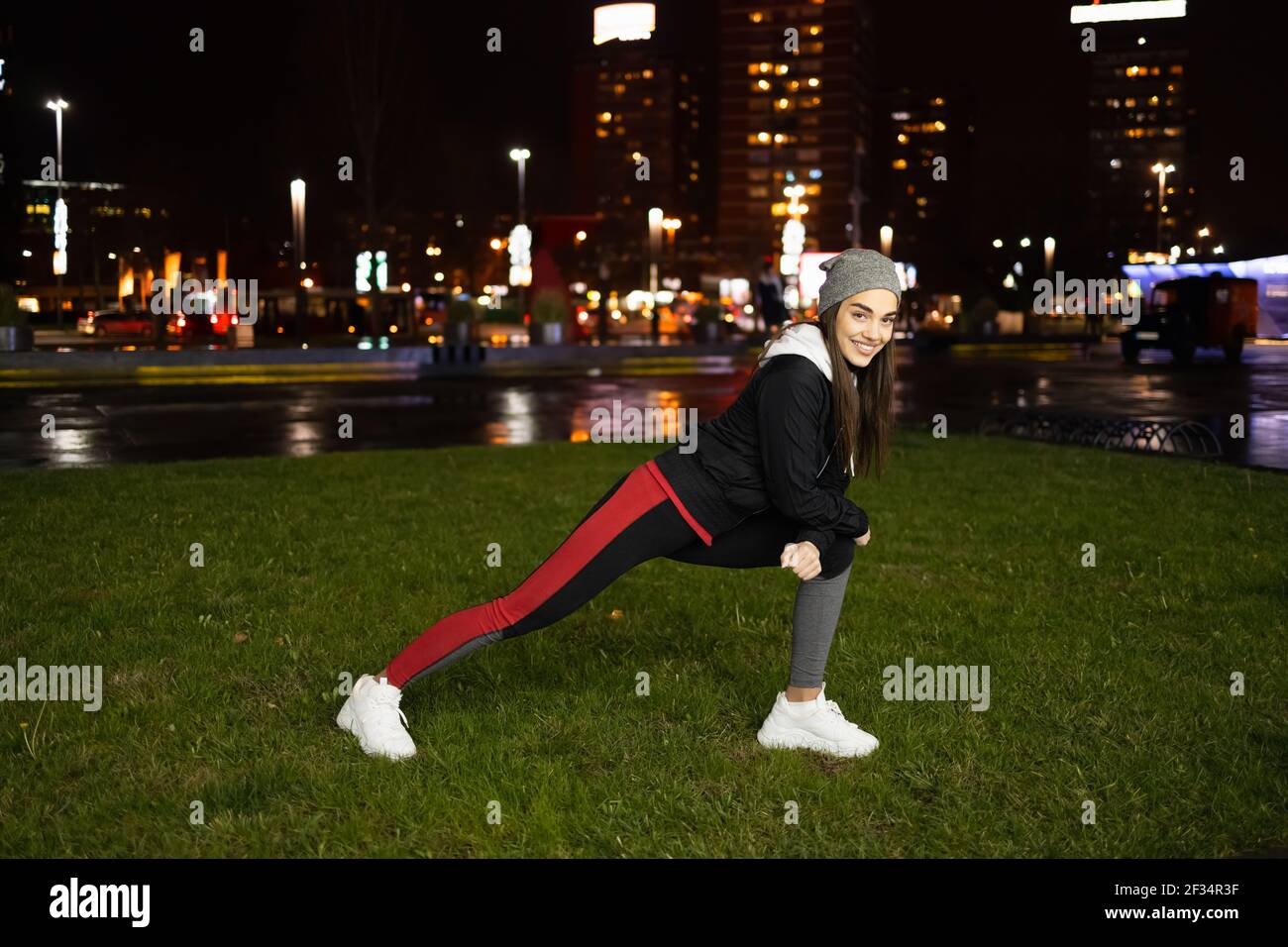 Donna che si stende dietro la gamba prima di una corsa serale Foto Stock