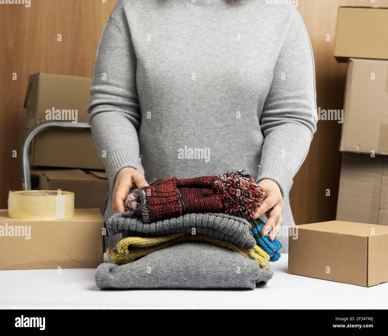donna in un maglione grigio raccoglie i vestiti in una scatola, concetto di assistenza e di volontariato, in movimento. Vendere cose non necessarie Foto Stock