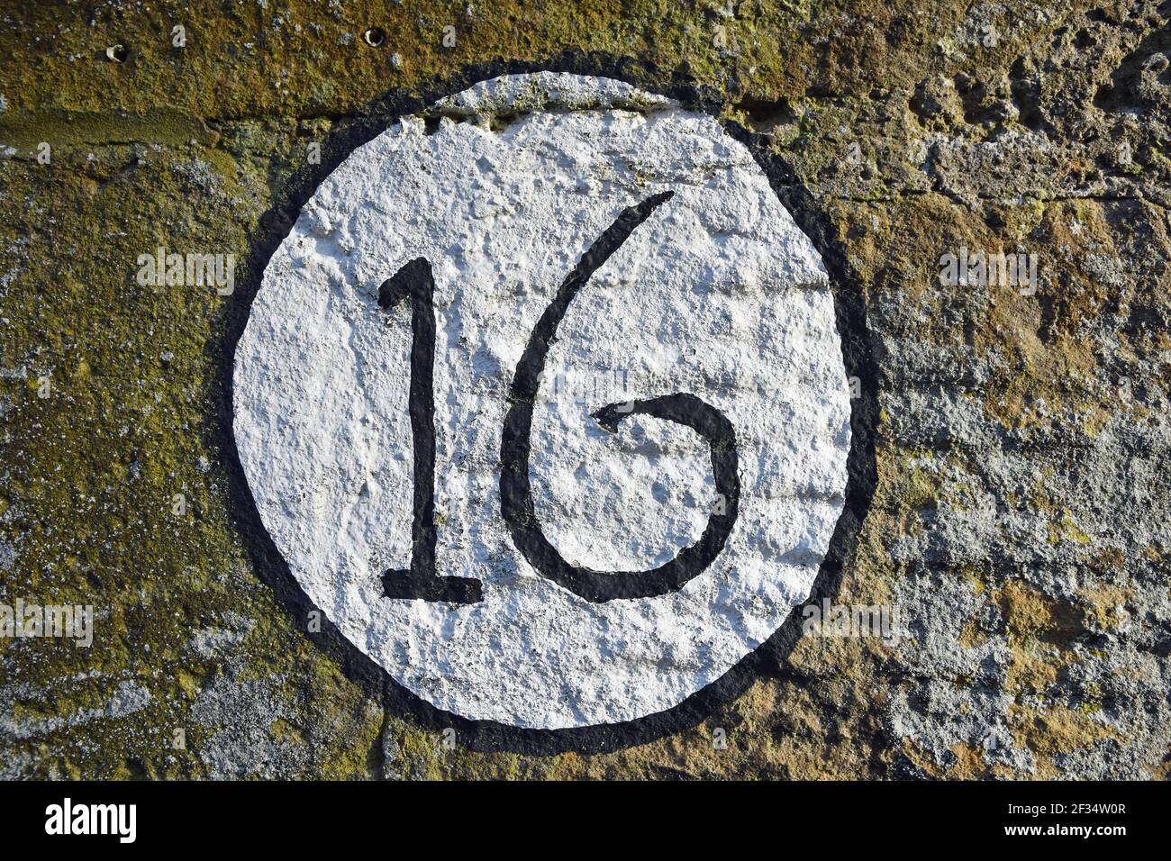Isolato dipinto numero 16 segno circolare su muro di pietra Foto Stock