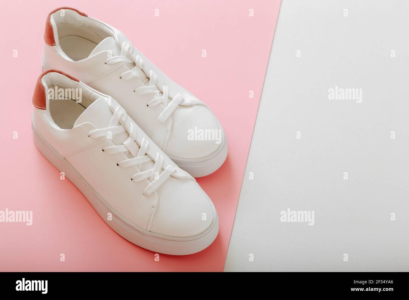 Sneakers bianche su sfondo rosa colorato. Scarpe donna in pelle bianca con lacci su sfondo rosa con spazio per la copia. Coppia di eleganti sneakers comfortabl Foto Stock