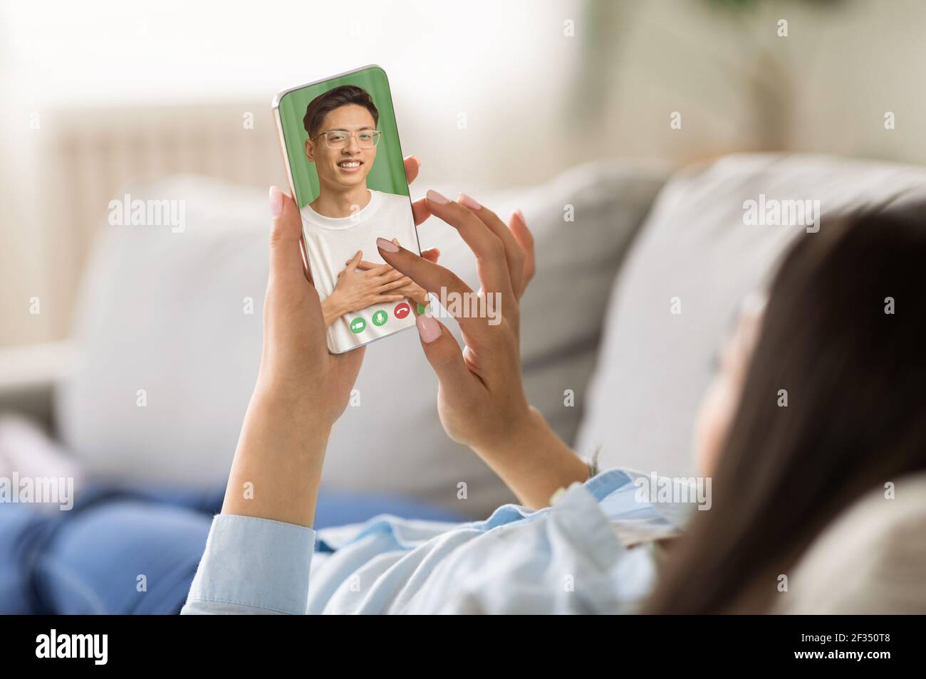 Chat online sullo schermo dello smartphone, relazioni remote durante il soggiorno e relax sul divano con il dispositivo Foto Stock