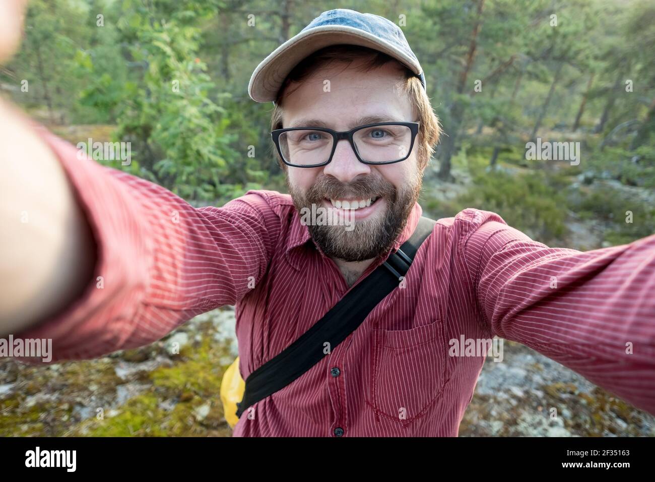Felice, sorridente uomo in un cappuccio e bicchieri fa un selfie, sullo sfondo della foresta. Attività ricreative. Foto Stock