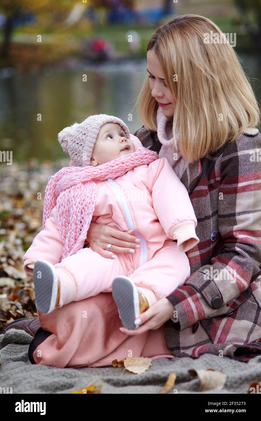 Bella bambina con madre seduta sulla plaid. Famiglia all'aperto. Adorabile bambina in abiti caldi al pic-nic in autunno parco il giorno di sole. Pret Foto Stock