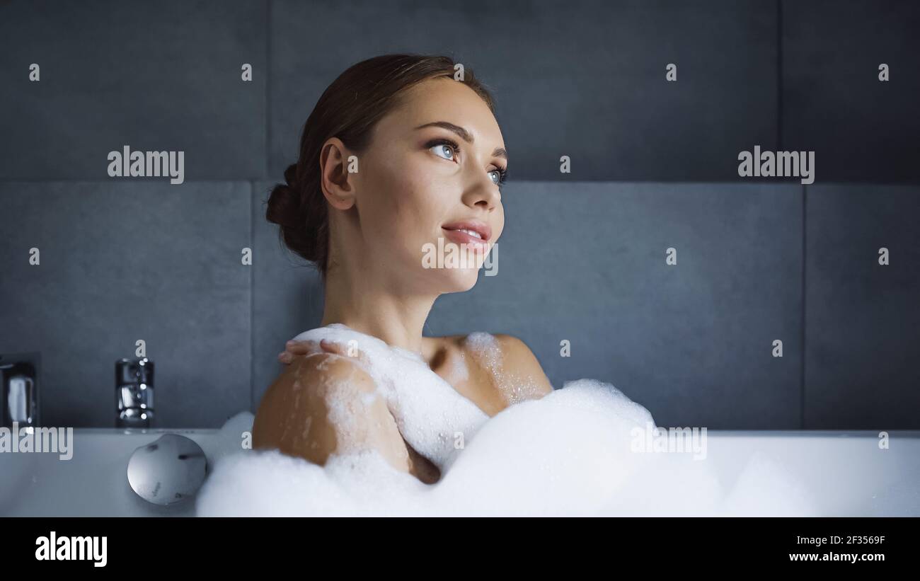 giovane donna sognante che prende il bagno con la schiuma nella vasca bianca Foto Stock