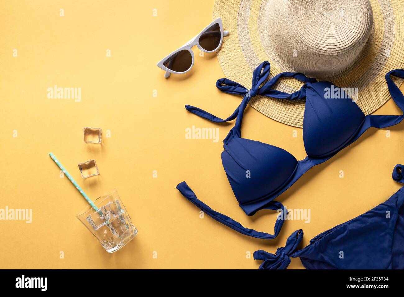 Tempo di divertimento estivo e accessori su sfondo giallo. Costume da bagno blu, cappello di paglia e occhiali da sole. Immagine orizzontale, posto per il testo Foto Stock