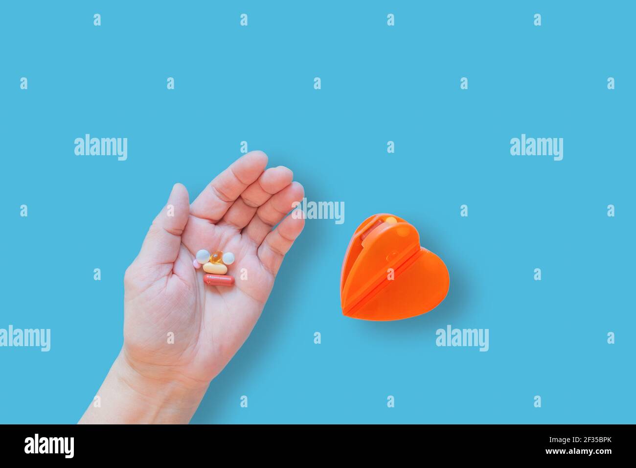 Varie pillole in mano e cuore forma scatola per la medicina su sfondo blu. Compresse mediche e capsule nel palmo della mano per il trattamento e scatola per Foto Stock