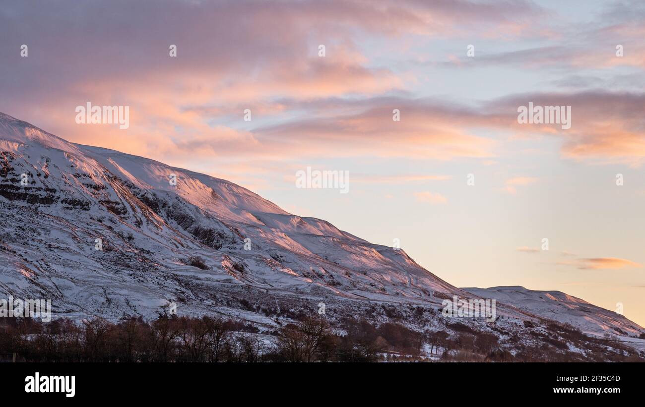 Un bagliore mattutino sulle colline invernali mentre il sole sorge sulle Campsie Fells dietro Lennoxtown, Scozia Foto Stock