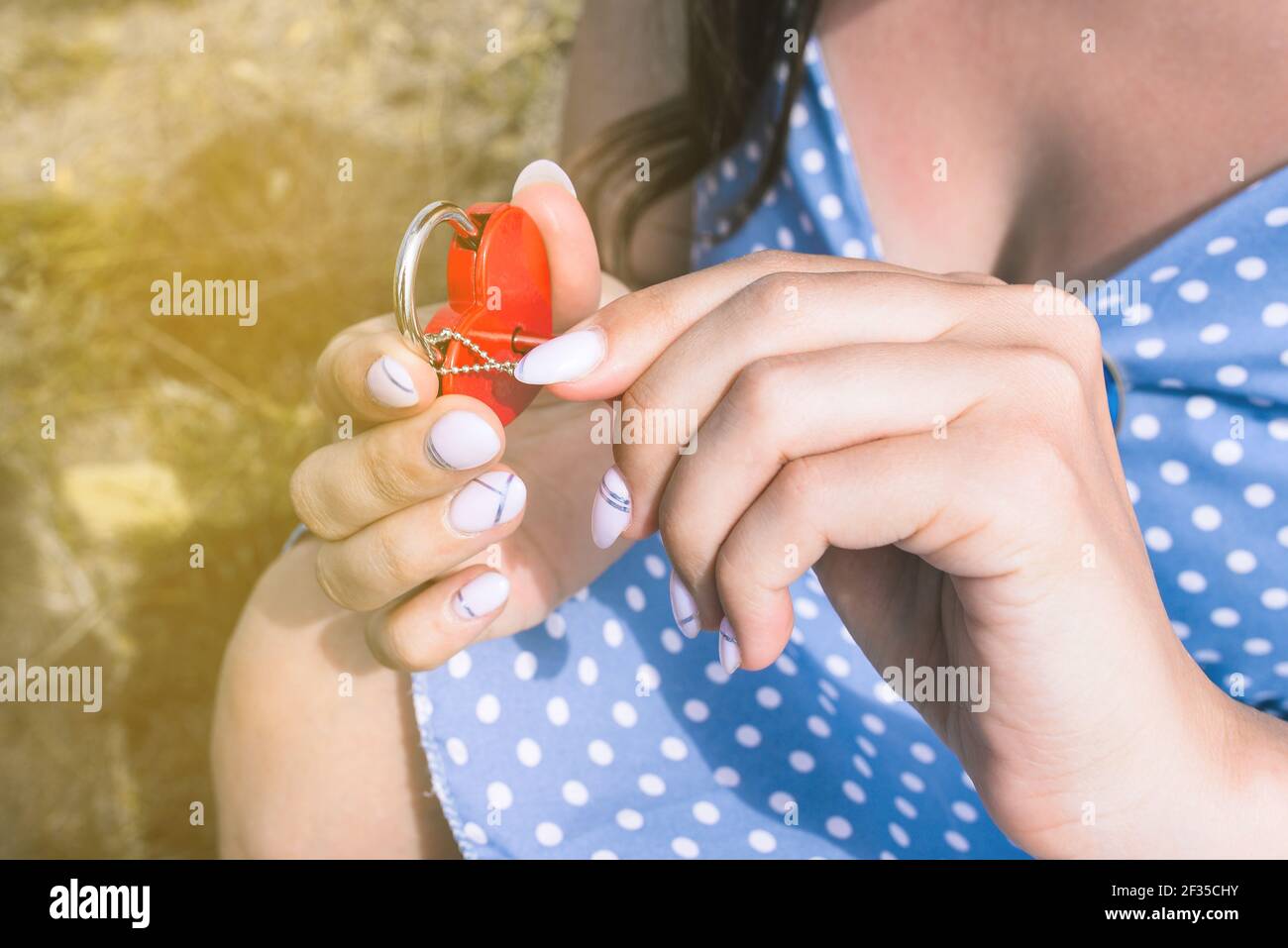 Giovane ragazza apre la serratura con una chiave. Lucchetto rosso a forma di cuore. Il concetto di datazione, rapporto e amore. Tradizioni degli sposi novelli. Foto Stock
