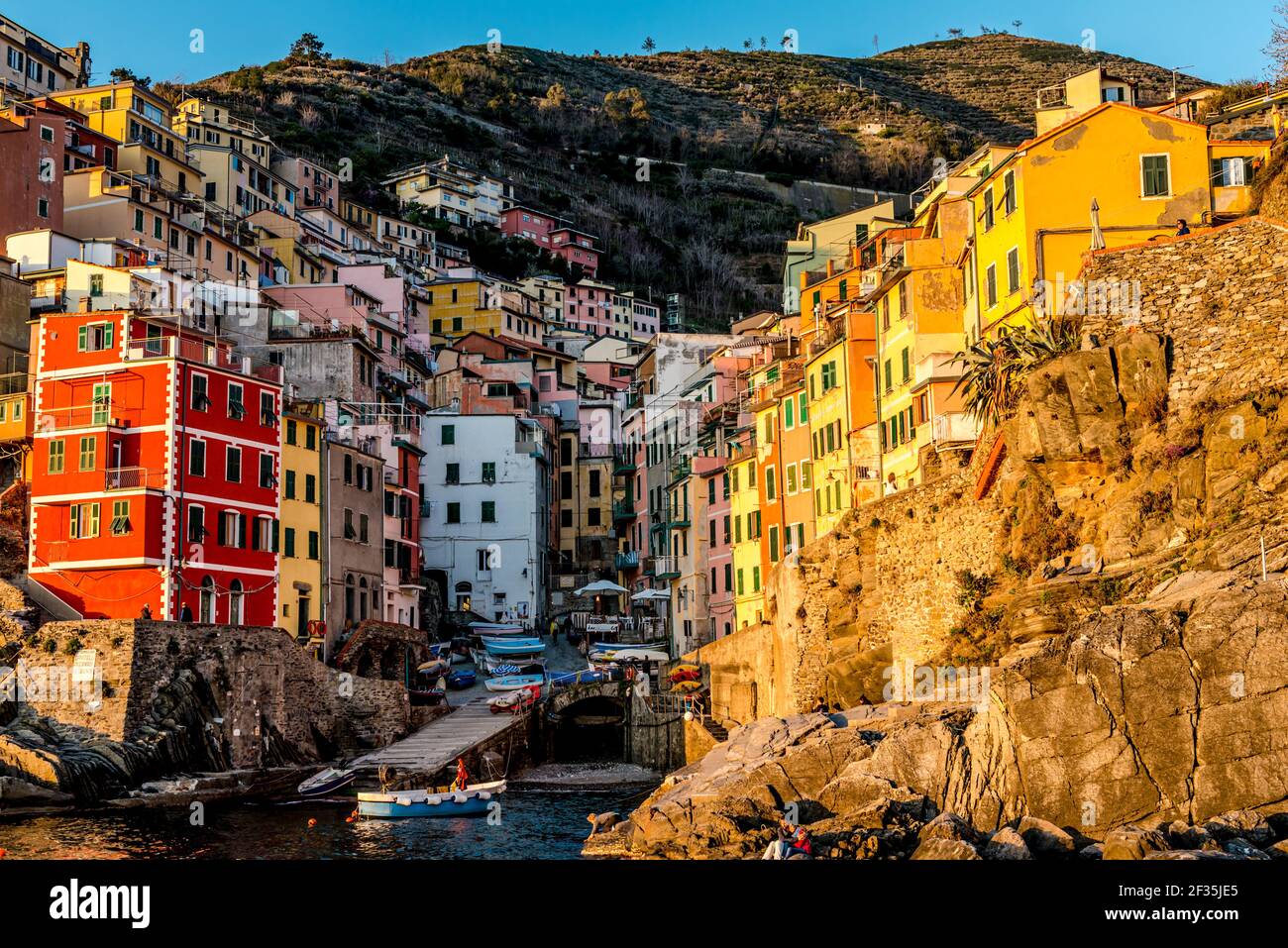 Vista ritagliata delle case colorate che circondano la strada in valle illuminata dal luminoso sole delle prime ore della sera. Villaggio di Riomaggiore, cinque Terre, Liguria, Italia. Foto Stock
