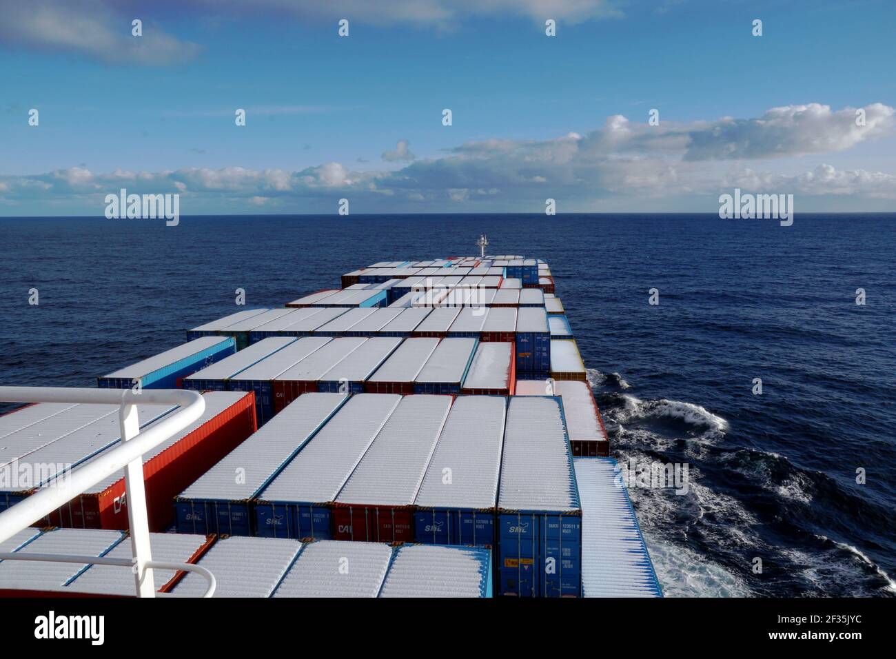 Nave container che naviga sull'oceano Pacifico in inverno, i container sono coperti da un sottile strato di neve. Vista dal ponte di navigazione. Foto Stock