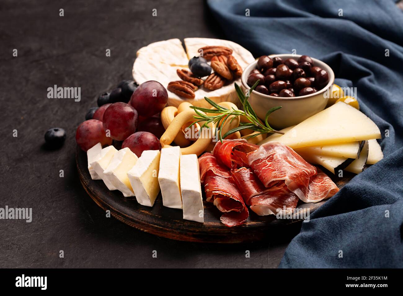 Salumi con jamon spagnolo, salsiccia di maiale con pepe, fuet, formaggio e frutti di bosco su sfondo scuro Foto Stock
