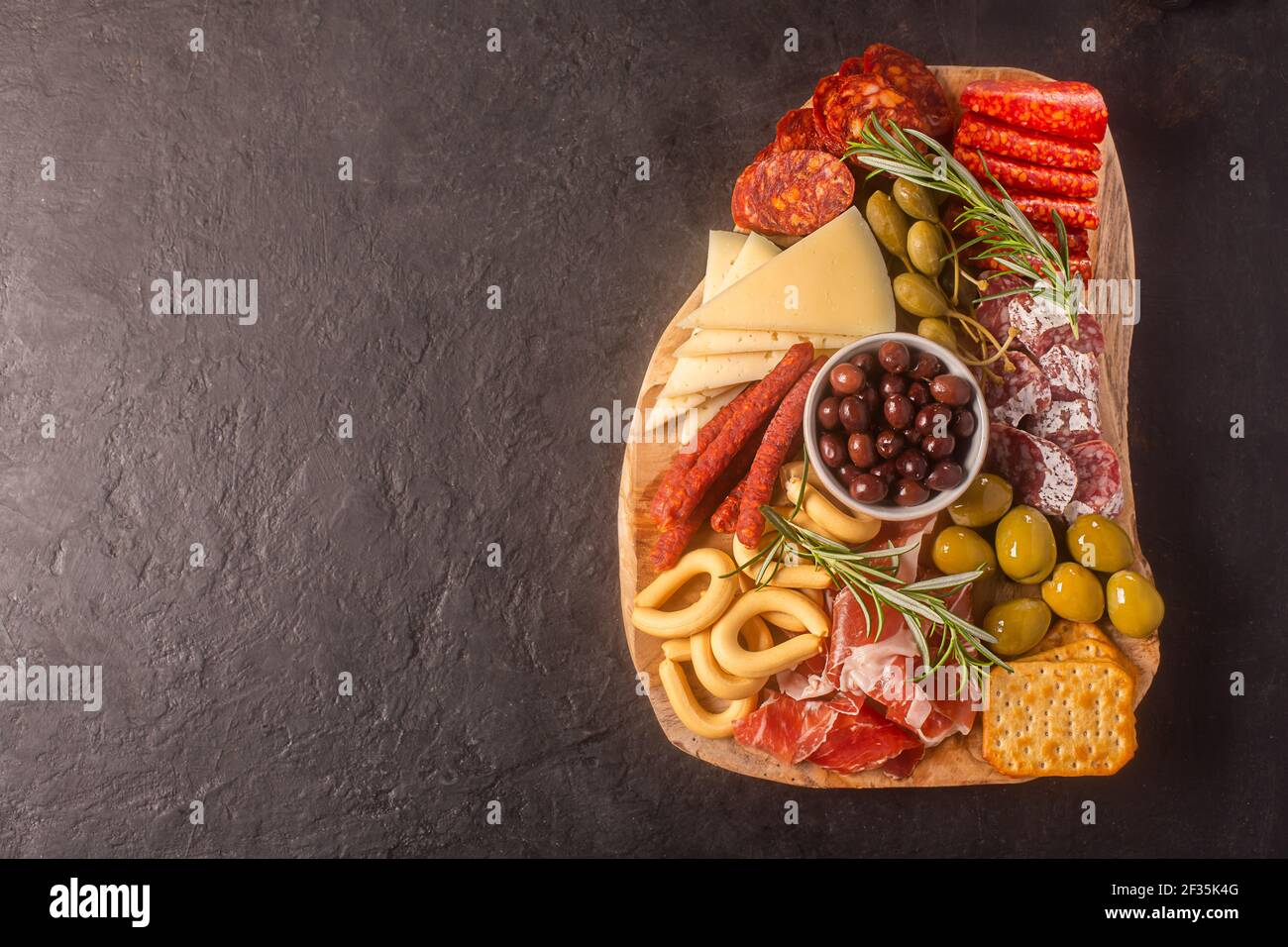 Salumi con jamon spagnolo, salsiccia di maiale con pepe, fuet, formaggio e frutti di bosco su sfondo scuro, vista dall'alto con spazio per la copia Foto Stock