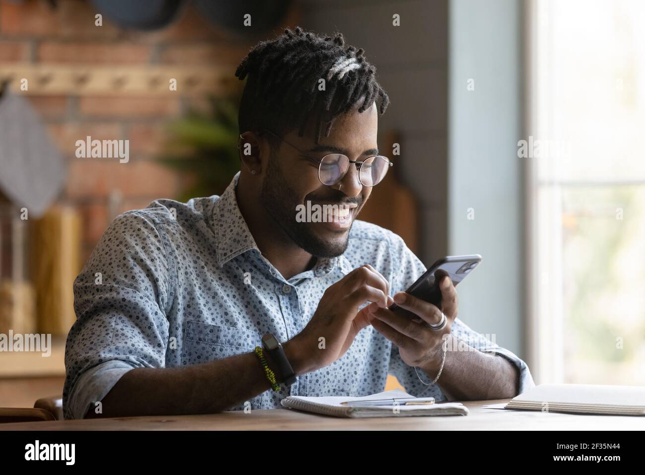 Felice giovane afroamericano uomo sedersi al tavolo uso telefono Foto Stock