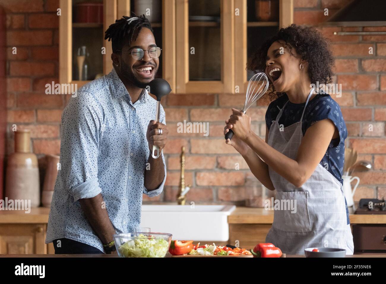 Giovane coppia africana cantare canzone in microfoni di utensili da cucina Foto Stock