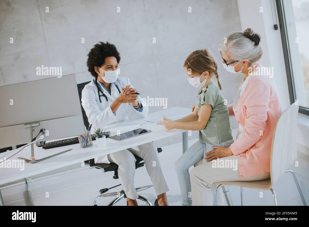 Nonna con maschere facciali protettive con nipotina carina nera medico femminile Foto Stock