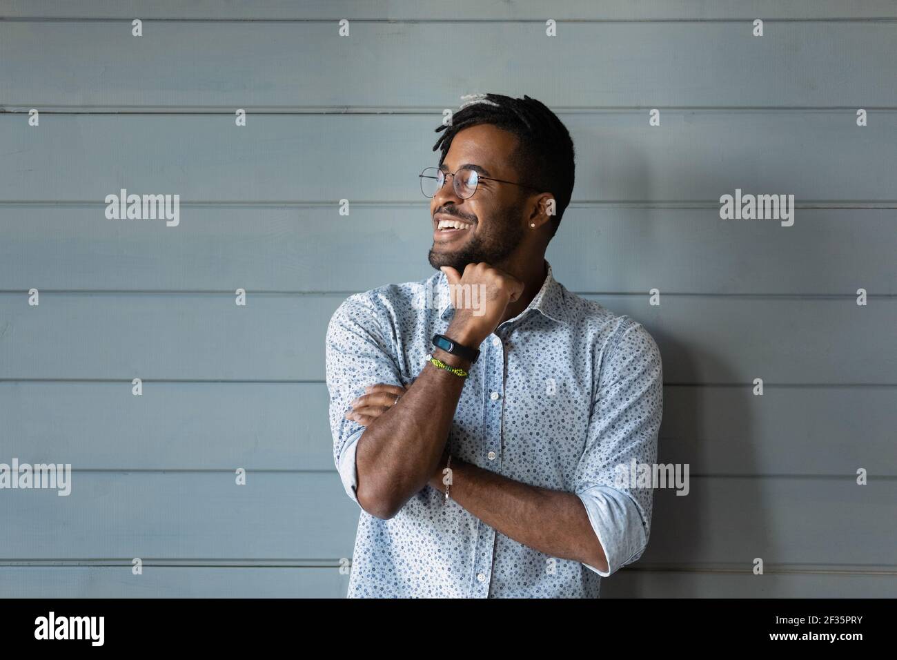 Sorridente uomo africano millenario in posa contro parete grigia guardare via Foto Stock