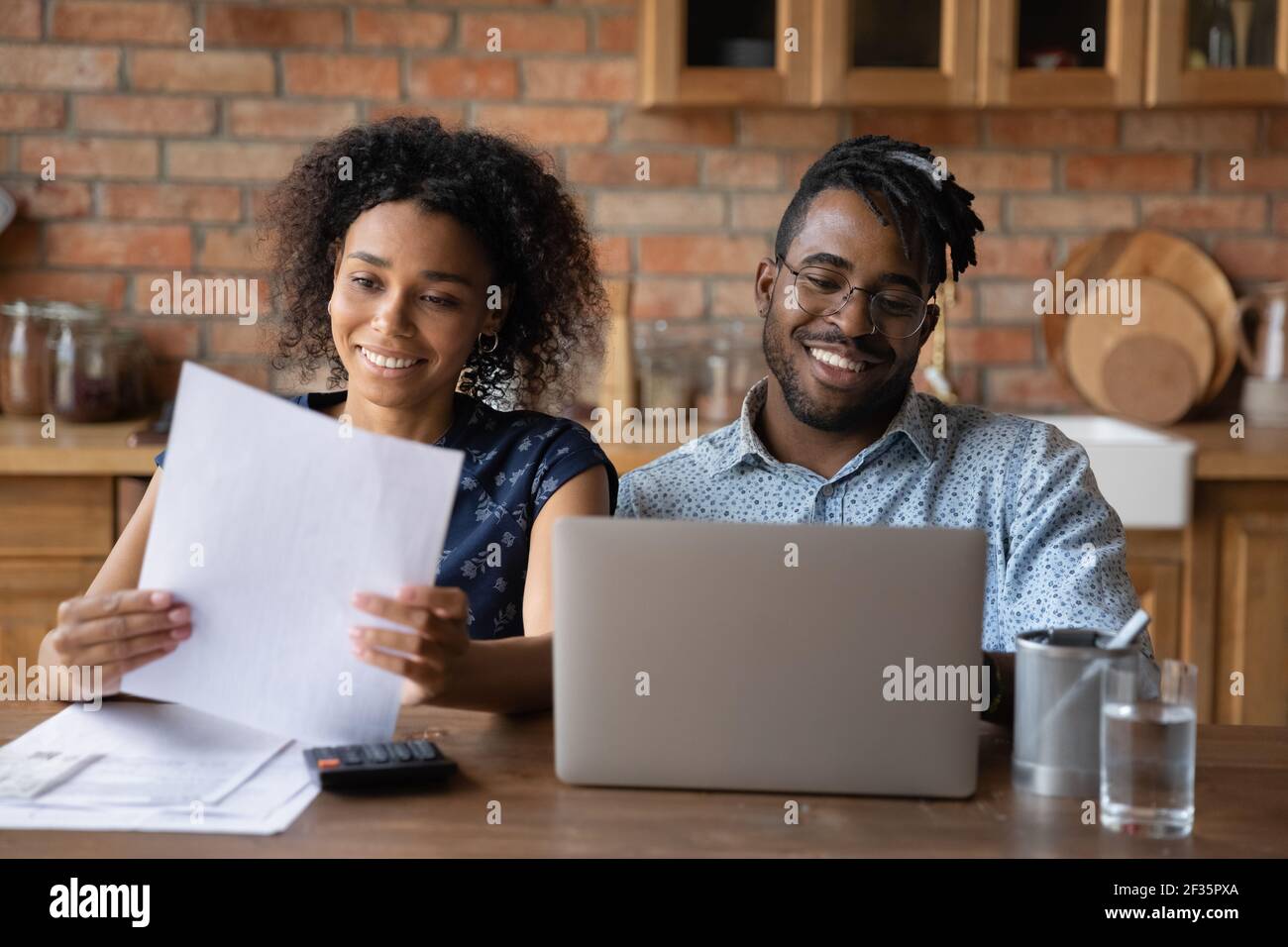 Felice coppia nera della famiglia impegnata nella contabilità domestica usando il laptop Foto Stock