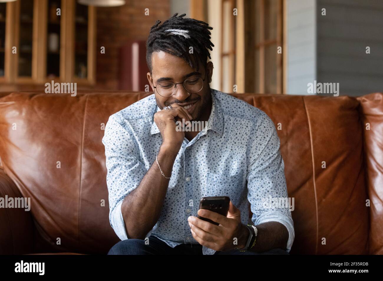 Felice ragazzo africano sedersi sul divano impegnato in gadget Foto Stock