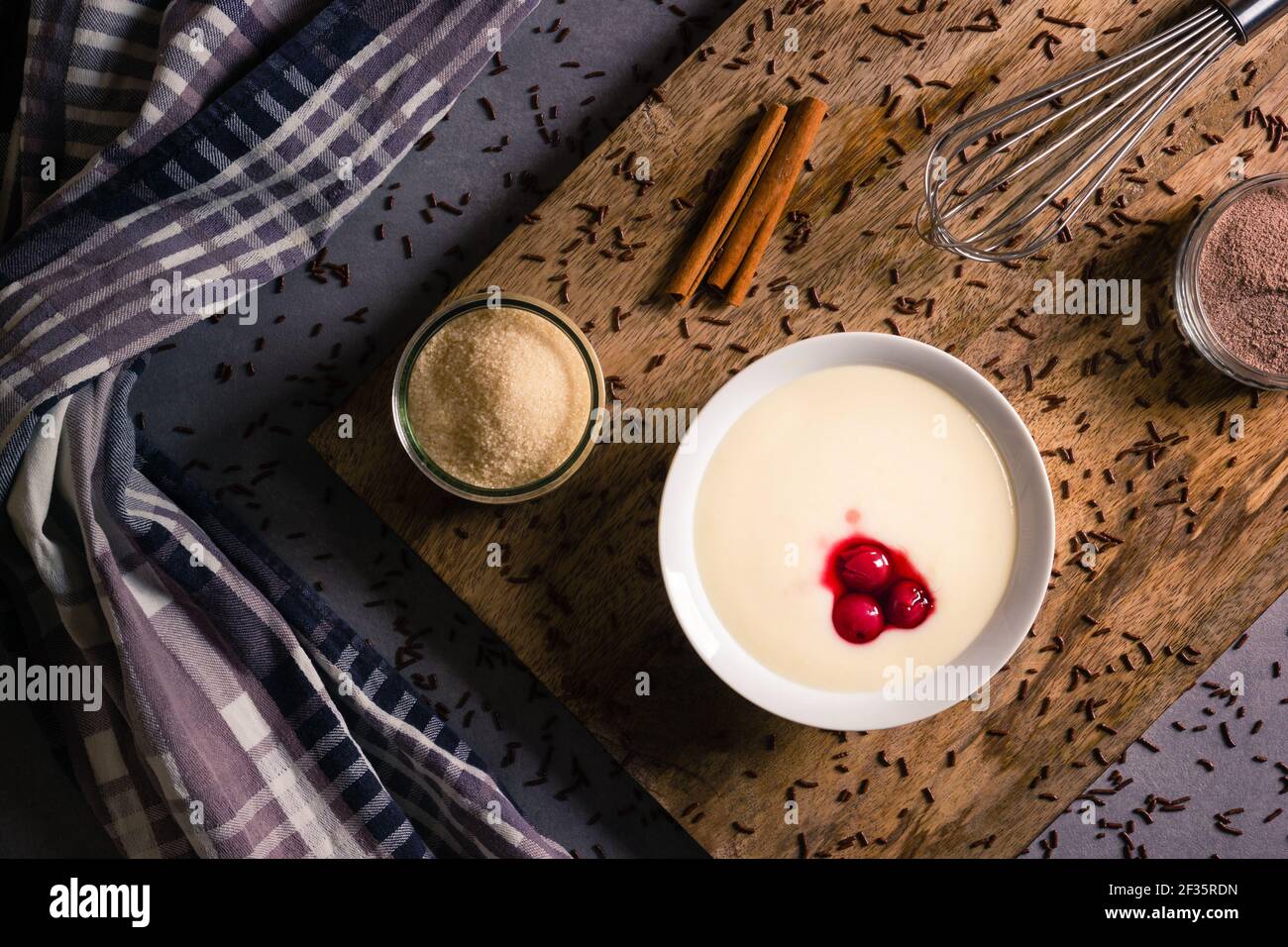 Porridge di semola con ciliegie oltre a bastoncini di cannella e spolverini di cioccolato su tavola di legno Foto Stock