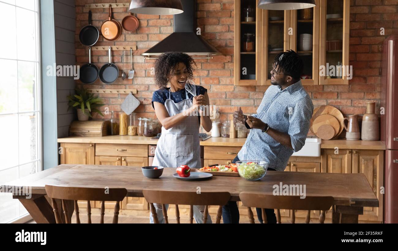 La gioiosa coppia nera millenaria si diverte in cucina cantando ad alta voce Foto Stock