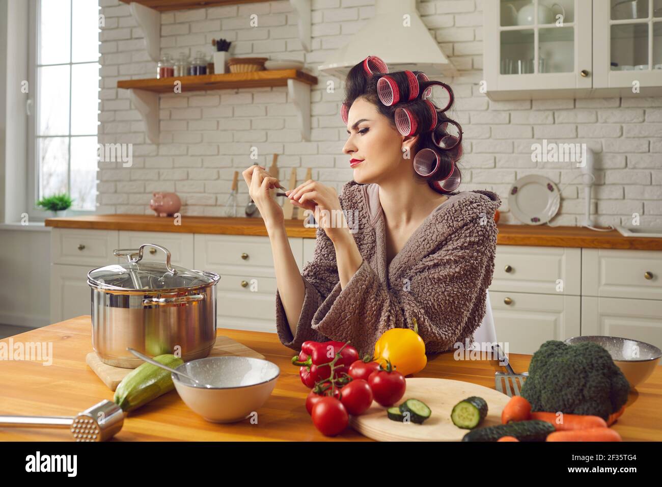 Bella giovane casalinga in capelli arricciatori limando le sue unghie seduta al tavolo da cucina Foto Stock