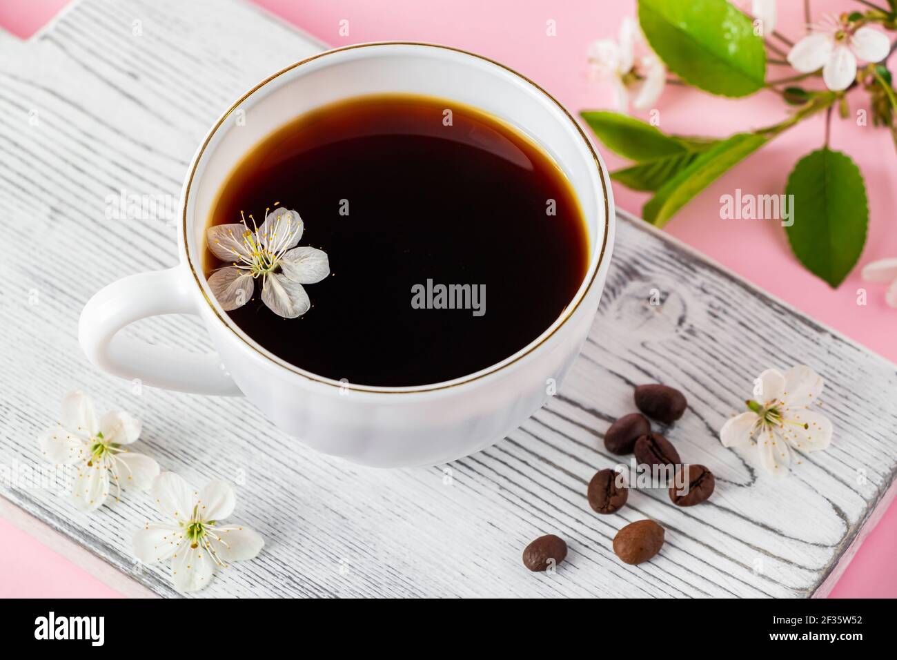 Tazza di caffè espresso forte e delicati fiori primaverili su sfondo rosa. Concetto di primavera e buon mattino. Foto Stock