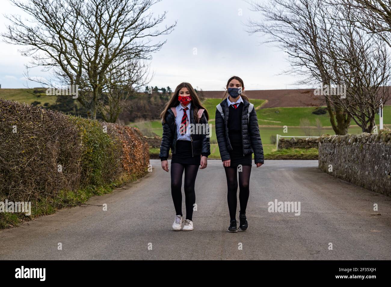 East Lothian, Scozia, Regno Unito, 15 marzo 2021. I bambini della scuola ritornano alla scuola secondaria: Gemelli, Louisa e Imogen, di 12 anni e in S1 sono tornati oggi per la prima volta al North Berwick High School dal recente blocco durante la pandemia del coronavirus, ma solo per 3 ore oggi per tutta la settimana, quando si scende dal bus scolastico a Kilduff Foto Stock