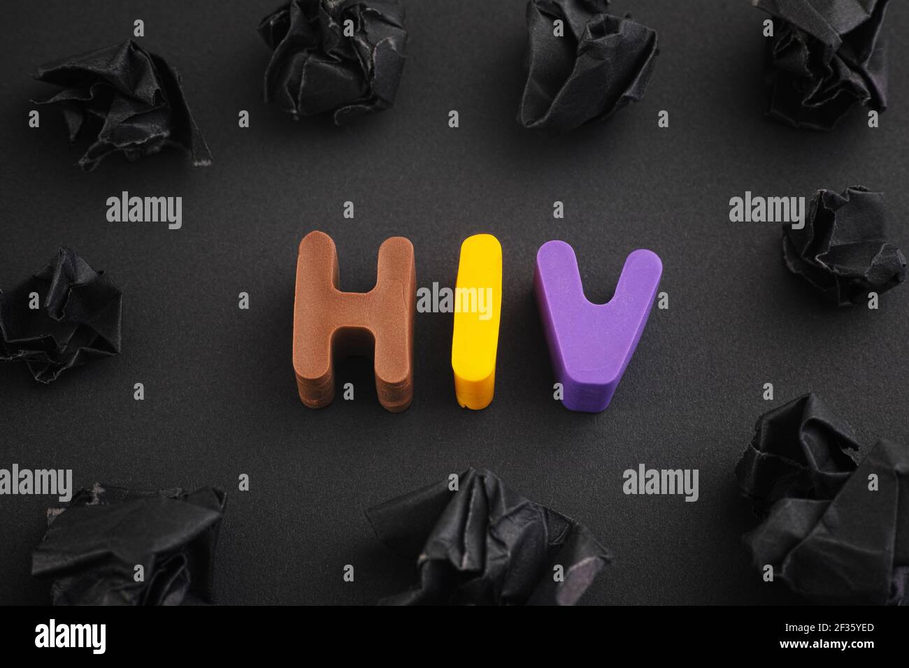 L'abbreviazione HIV è composta da lettere di argilla polimerica con alcune palle di carta nera sbriciottita intorno ad essa. Primo piano. Foto Stock